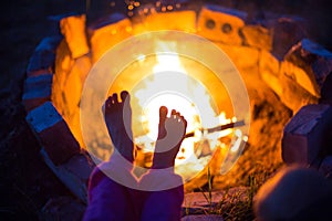 Bare feet of child by fire. Gatherings at night by campfire in open air in summer in nature. Family camping trip, gatherings