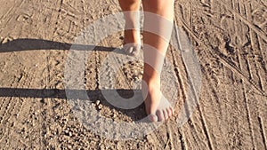 Bare feet of a child girl walk along a country road in summer in sunny clear weather. Children`s rest in the countryside in the