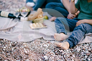 Bare feet of a child sitting on a bedspread on a pebble beach with parents