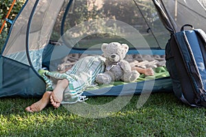 bare feet of a child sleeping lying on his stomach in a tent with his favorite teddy bear