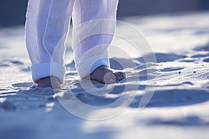 Bare feet of a child in white pants on the sand