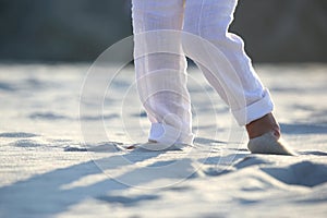 Bare feet of a child in white pants on the sand