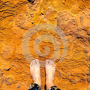 Bare feet for comaprison with orange mineral of natural water spring in Damia
