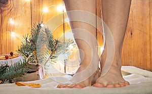 Bare feet on the floor on a white carpet near the New Year tree with gifts and garlands, in anticipation