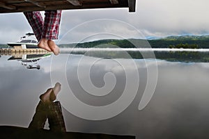 Bare feet hanging from a wooden pier above the water, with space for text design. Enjoying the sunrise over the misty