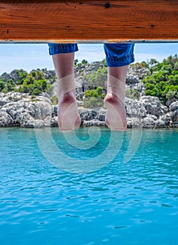 Bare feet hanging from wooden pier sea water. Holiday vacation by the sea