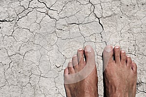 Bare feet of a man on a cracked dry soil