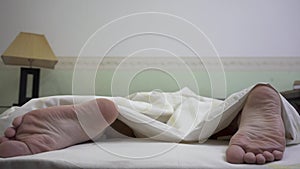 Bare feet men sticking out from under the blanket close up. The man tossing and turning in sleep. Morning time of young