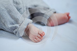 Bare feet of a newborn baby in a grey tucked up pants, selective focus