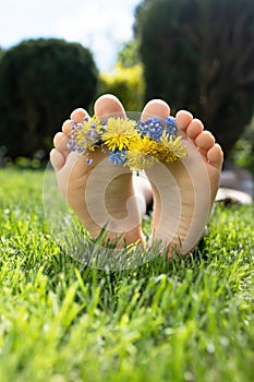 bare feet ofchild lying on bright juicy green grass. wreath of yellow-blue field flowers lies on the toe