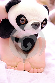 Bare feet, relaxing with panda toy. Lazy holiday concept. Waking up. Happy childhood