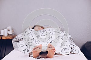 Bare feet of a teenage girl. The girl is lying on the bed covered with a blanket. Foot and heel