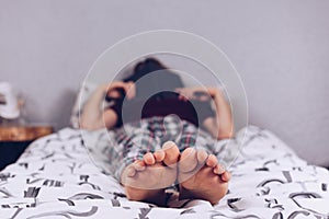 Bare feet of a teenage girl. The girl in pajamas lies on the bed covered with a blanket. Foot