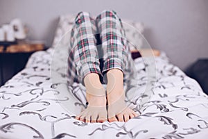 Bare feet of a teenage girl. The girl in pajamas lies on the bed covered with a blanket. Foot