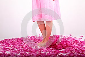 Bare feet of teenage girl standing on pink petals by bouquet of peonies