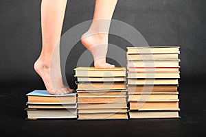 Bare feet of teenage girl stepping on old books