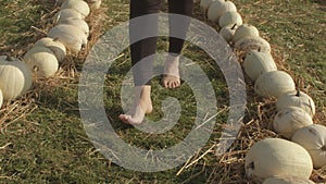 Bare feet walk on the grass. White pumpkins decorate the path.
