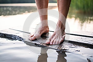 Bare feet of woman standing by lake outdoors before swimming.