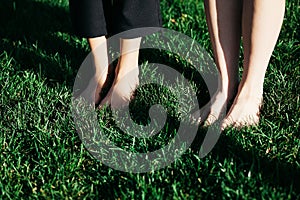 Bare feet of young girls stand barefoot in the dense green grass