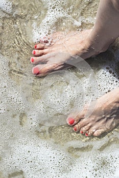 Bare female feet on the shore washed by the sea