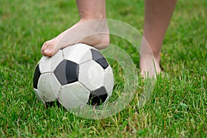 Bare foot of a girl on the soccer ball in green grass