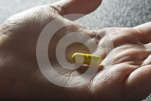 Bare hand holding one yellow medicinal tablet