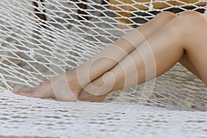 Bare legs of a woman in a white hammock on a tropical beach. Travel and vacation