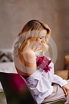 bare shoulders. a blonde woman in a white shirt and a bouquet of peonies.