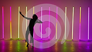 A barefoot actress performs contemp against the backdrop of multicolored neon tubes. A ballerina dances plastically