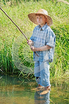 Barefoot angler boy fishing standing in transparent freshwater pond