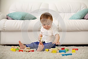 Barefoot baby sits on carpet and plays with wooden