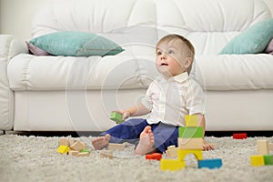 Barefoot baby sits on carpet with wooden cubes and