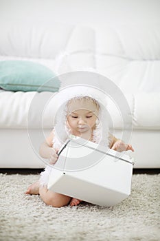 Barefoot baby in white soft hat sits on carpet