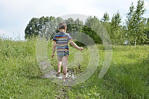 Barefoot boy runs through a puddle.