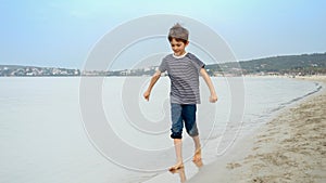 Barefoot boy runs on a sandy beach, splashing water, carefree spirit of childhood, travel, and the pursuit of happiness and