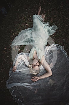 Barefoot bride lie on gras and leaves with veil around her