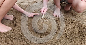 Barefoot children build sand structure banging wooden stick