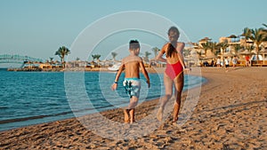 Barefoot children having fun at seashore in sunset. Sibling running on sea beach