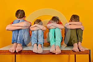 Barefoot children sit with their legs crossed and hugging their knees. Four children lowered their heads down