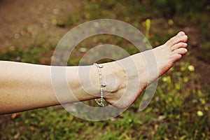 Barefoot with fashionable boho anklet on the grass background