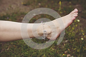 barefoot with fashionable boho anklet on the grass background