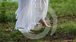 Barefoot feet girl in white dress walking on green grass