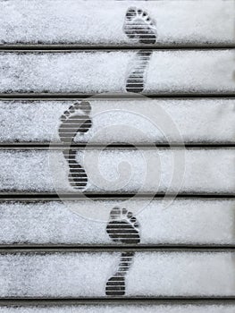 Barefoot footprints close up on wooden jetty with clear white snow in winter