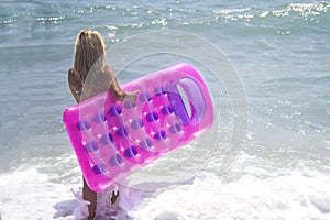 Barefoot girl in blue bikini at the sea. Slim tall girl in swimwear walking in the sea with pink inflatable pool raft