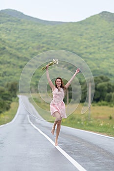 Barefoot girl with chamomile bouquet running along road after ra
