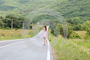 Barefoot girl with chamomile bouquet running along road after ra