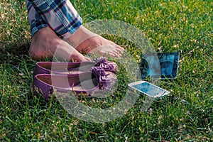 Barefoot girl relaxing on grass cross-legged with tablet-pc and smartphone