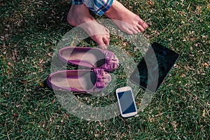 Barefoot girl sitting on grass with tablet-pc and smartphone