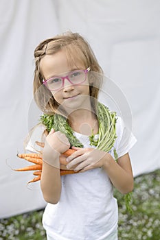 A barefoot girl stands on the green grass and tastes a juicy carrot