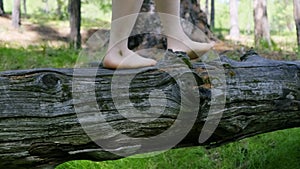 A barefoot girl walks on a log. Close-up